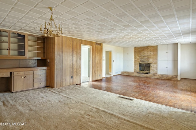 unfurnished living room with wooden walls, visible vents, carpet, a fireplace, and a notable chandelier