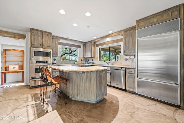 kitchen featuring a center island, light stone counters, backsplash, built in appliances, and a kitchen bar