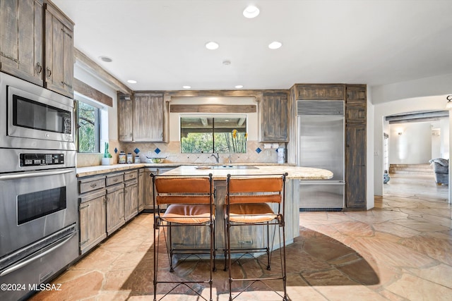 kitchen with built in appliances, decorative backsplash, a center island, and a breakfast bar area