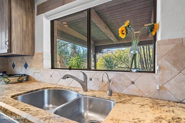 kitchen with tasteful backsplash, light stone counters, sink, and beam ceiling