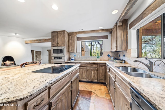 kitchen featuring backsplash, sink, light stone countertops, a fireplace, and appliances with stainless steel finishes