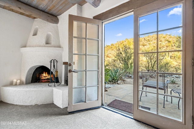 doorway to outside with beam ceiling, a large fireplace, carpet, and wood ceiling