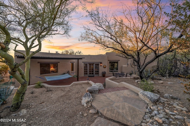 back house at dusk featuring french doors and a patio