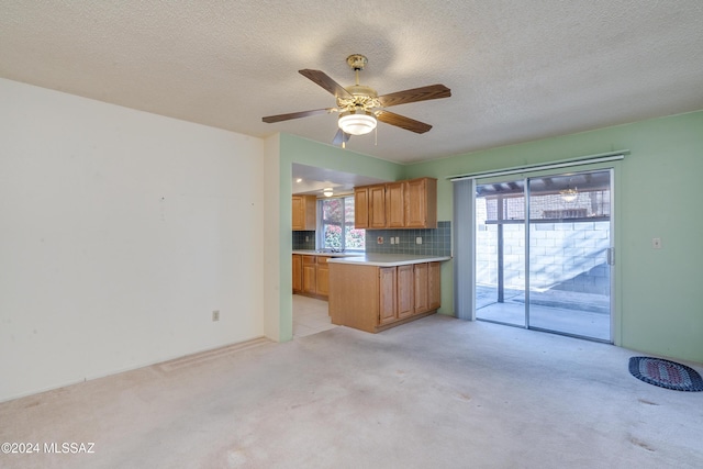 kitchen with a textured ceiling, light colored carpet, light countertops, brown cabinets, and tasteful backsplash