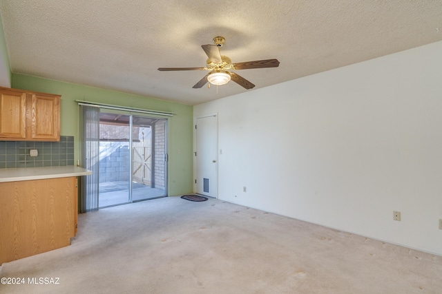 interior space with tasteful backsplash, light countertops, a ceiling fan, light carpet, and a textured ceiling