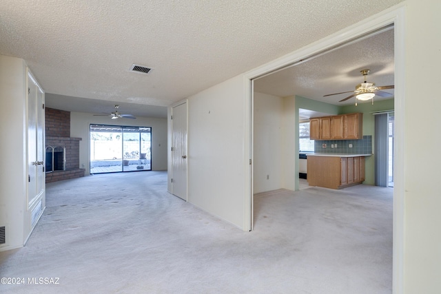 unfurnished living room featuring a ceiling fan, light colored carpet, a fireplace, and visible vents