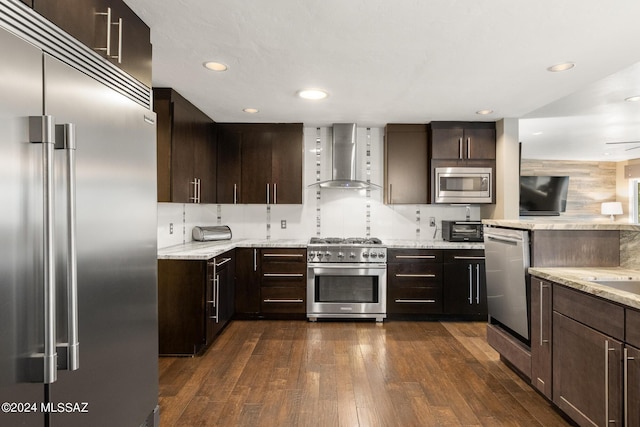 kitchen with light stone countertops, dark wood-type flooring, wall chimney exhaust hood, and built in appliances