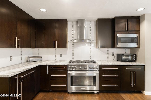 kitchen with light stone countertops, wall chimney exhaust hood, stainless steel appliances, and dark brown cabinets