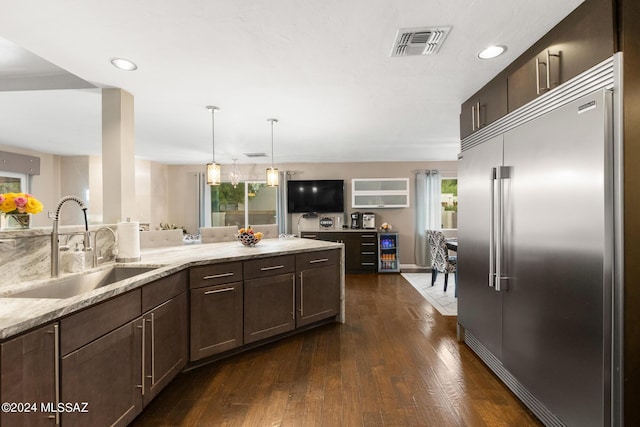 kitchen featuring light stone countertops, decorative light fixtures, dark wood-type flooring, stainless steel built in refrigerator, and sink