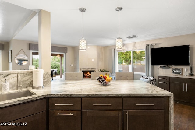 kitchen featuring decorative light fixtures, a large fireplace, sink, dark brown cabinetry, and a healthy amount of sunlight