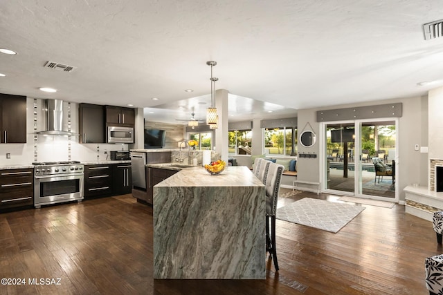 kitchen featuring appliances with stainless steel finishes, decorative backsplash, wall chimney range hood, dark brown cabinetry, and sink