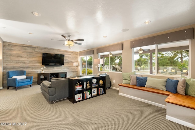 living room featuring ceiling fan, wood walls, and carpet flooring