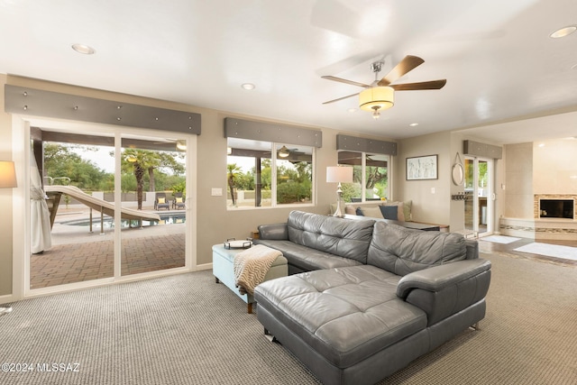 carpeted living room with ceiling fan and a stone fireplace