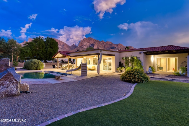 back house at dusk featuring a mountain view, a lawn, and a patio