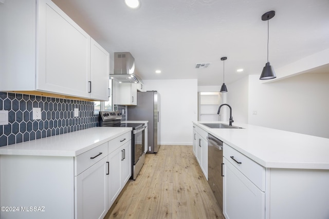 kitchen featuring wall chimney range hood, sink, hanging light fixtures, white cabinetry, and stainless steel appliances