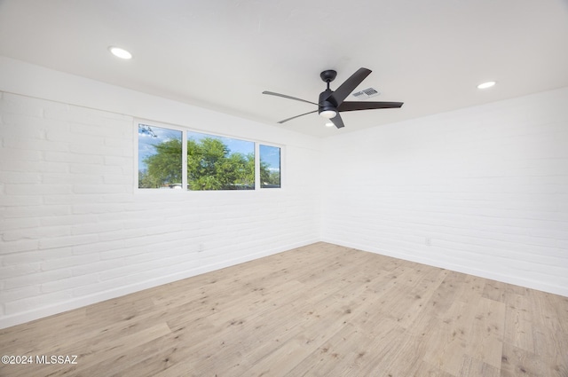 unfurnished room with light hardwood / wood-style flooring, ceiling fan, and brick wall