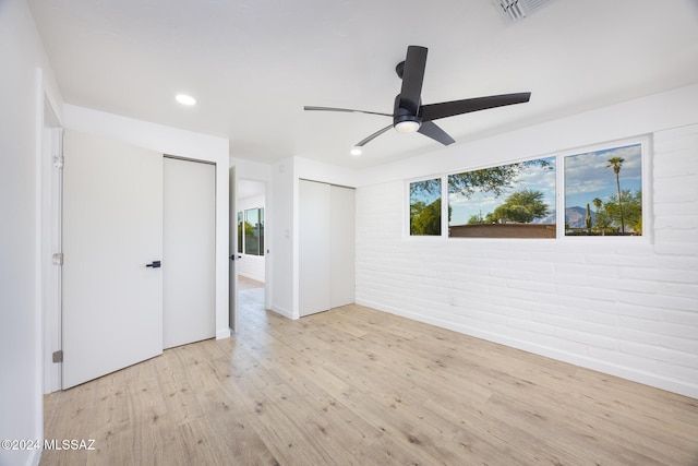 unfurnished bedroom featuring ceiling fan, brick wall, and light wood-type flooring