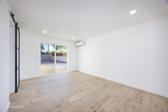 empty room with an AC wall unit, a barn door, and light hardwood / wood-style floors