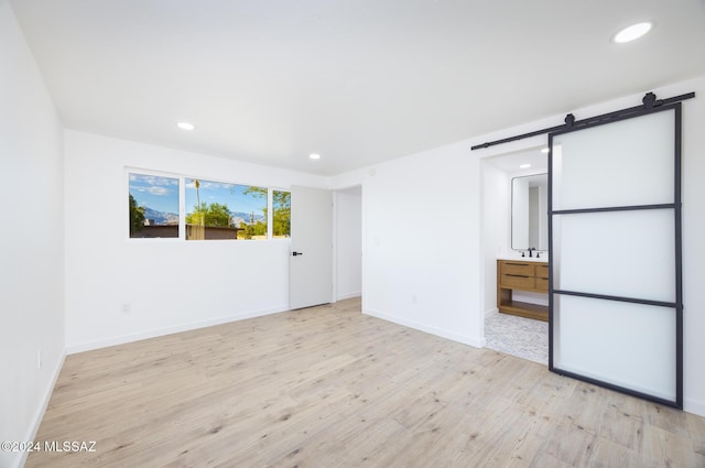 unfurnished room featuring a barn door, light hardwood / wood-style flooring, and sink