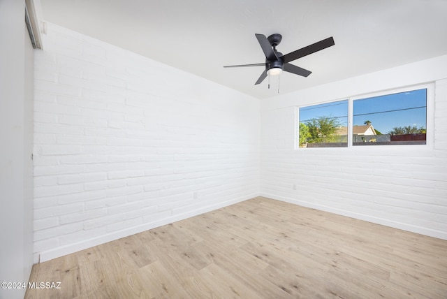 empty room with light hardwood / wood-style floors, ceiling fan, and brick wall