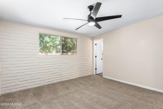 empty room featuring ceiling fan, carpet floors, and brick wall