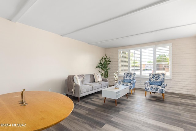 living room featuring beamed ceiling, dark wood-type flooring, and brick wall