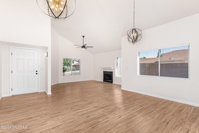 unfurnished living room featuring ceiling fan with notable chandelier, light wood-type flooring, and high vaulted ceiling