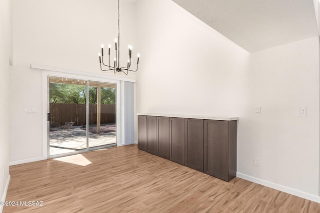 unfurnished dining area featuring light hardwood / wood-style flooring, high vaulted ceiling, and a chandelier