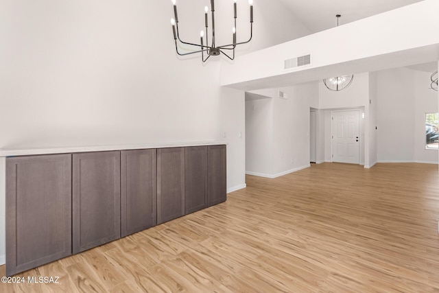 empty room featuring high vaulted ceiling, a chandelier, and light wood-type flooring