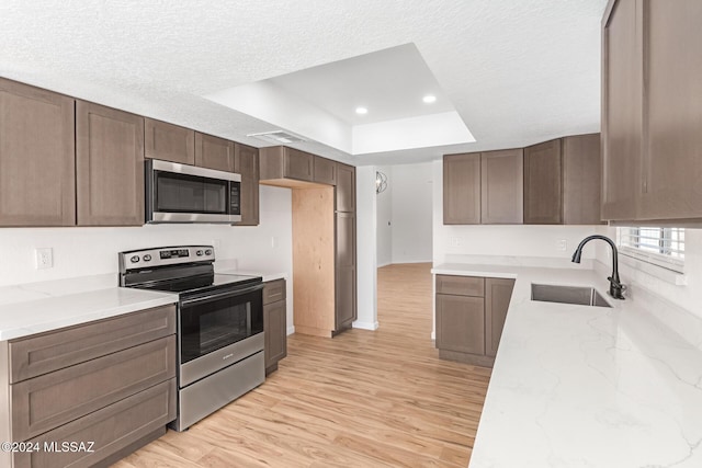 kitchen with sink, stainless steel appliances, a raised ceiling, light hardwood / wood-style floors, and a textured ceiling