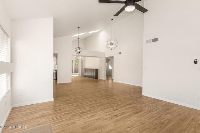 unfurnished living room featuring wood-type flooring, ceiling fan with notable chandelier, and high vaulted ceiling