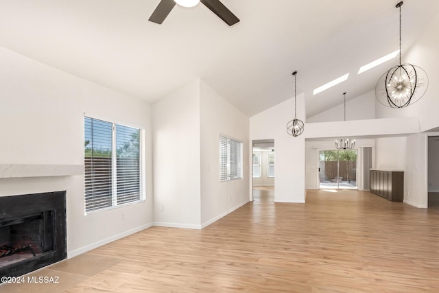 unfurnished living room with high vaulted ceiling, ceiling fan with notable chandelier, and light wood-type flooring