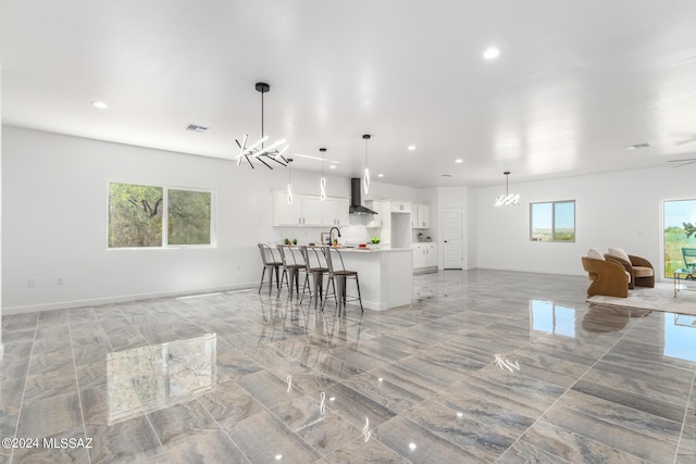 kitchen with pendant lighting, a breakfast bar, white cabinets, wall chimney exhaust hood, and an island with sink