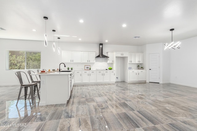 kitchen with a kitchen bar, decorative light fixtures, white cabinetry, and wall chimney exhaust hood