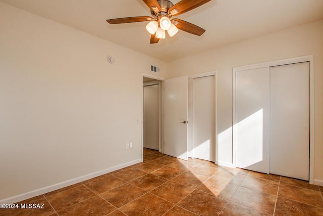 unfurnished bedroom with dark tile patterned flooring, ceiling fan, and multiple closets