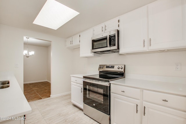 kitchen featuring a skylight, white cabinets, stainless steel appliances, and decorative light fixtures