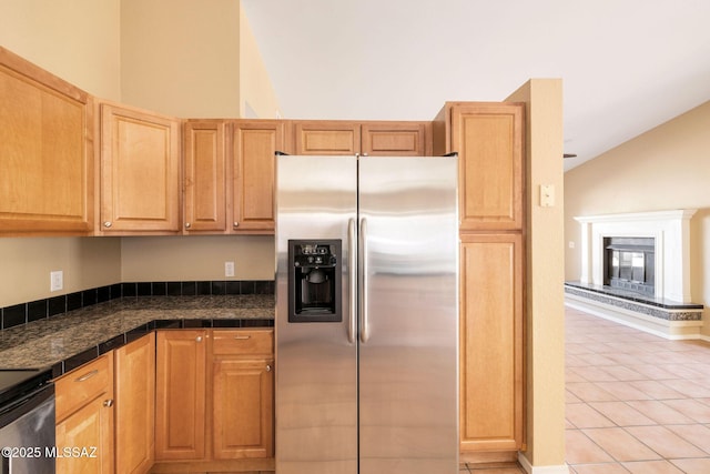 kitchen featuring lofted ceiling, stainless steel refrigerator with ice dispenser, light tile patterned flooring, and range