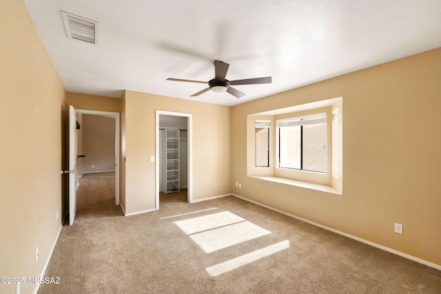 unfurnished bedroom featuring ceiling fan, light colored carpet, a closet, and a spacious closet