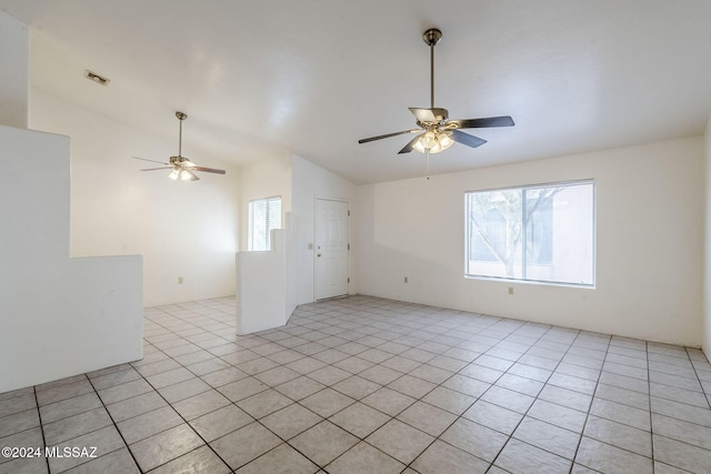 spare room featuring vaulted ceiling, light tile patterned floors, visible vents, and a ceiling fan