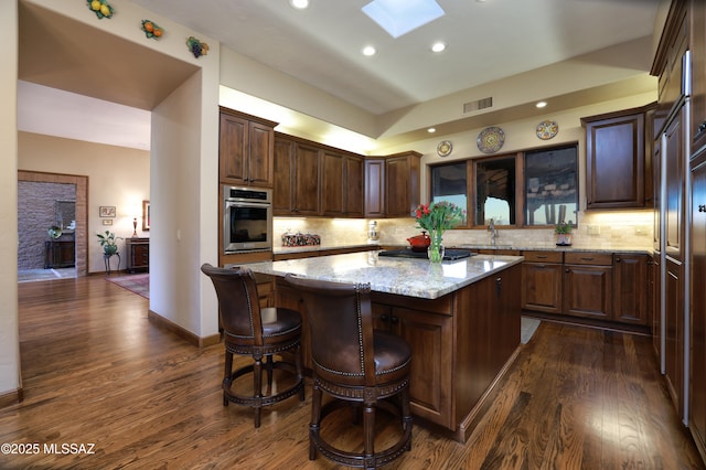 kitchen with a skylight, a center island, light stone counters, dark hardwood / wood-style floors, and oven