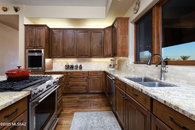 kitchen with appliances with stainless steel finishes, light stone countertops, dark wood-type flooring, sink, and tasteful backsplash