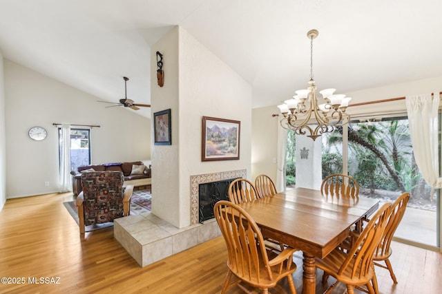 dining space with a tiled fireplace, lofted ceiling, light hardwood / wood-style floors, and ceiling fan with notable chandelier