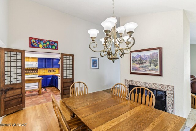 dining space with light hardwood / wood-style floors, a tile fireplace, and an inviting chandelier