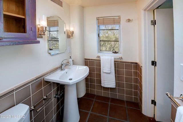 bathroom with toilet, tile patterned floors, and tile walls