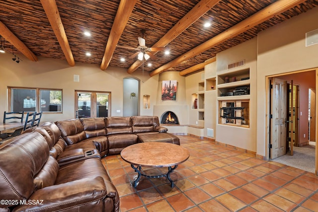 living room with tile patterned flooring, built in shelves, ceiling fan, a fireplace, and beamed ceiling