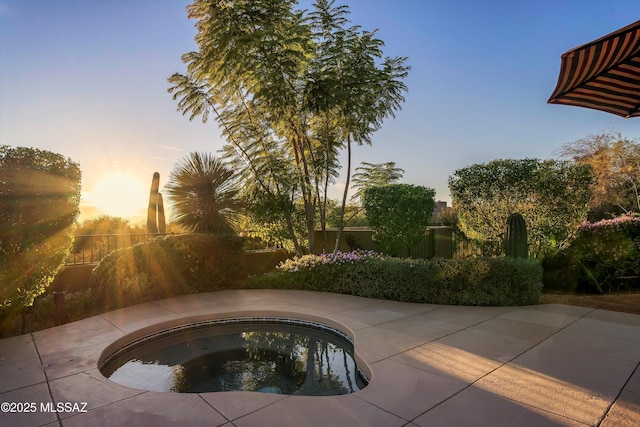 pool at dusk with an in ground hot tub and a patio