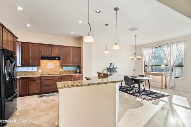 kitchen with black appliances, light stone countertops, hanging light fixtures, and a kitchen island with sink