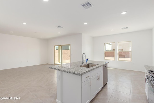 kitchen with white cabinetry, sink, light stone countertops, stainless steel appliances, and an island with sink