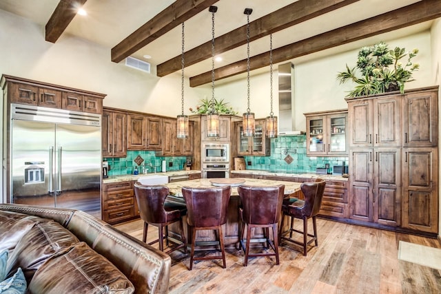 kitchen featuring a center island, light stone counters, built in appliances, pendant lighting, and a breakfast bar