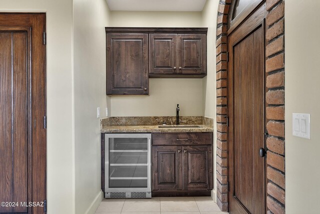 bar with dark brown cabinetry, beverage cooler, sink, light tile patterned floors, and stone counters